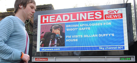 Pedestrians pass a large advertising screen showing a news story about Britain's Prime Minister Gordon Brown in London April 28, 2010. Britain's Prime Minister Gordon Brown was caught on tape describing a voter as "a bigoted woman" on Wednesday after she confronted him on immigration and the economy in an election campaign walkabout in northern England. Brown made the unguarded comment in his car as he drove away away from a visit designed to bring him into closer contact with the broader public rather than carefully staged party meetings. His Labour Party trails the opposition Conservatives and, in some polls, the third force Liberal Democrats. REUTERS/Toby Melville (BRITAIN - Tags: ELECTIONS POLITICS)