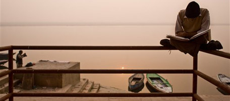 A man reads a newspaper while sitting on the railing in front of the Ganges River, January 2008 in Varanasi, India. The ancient city of Varanasi is one of the top Hindu pilgrimage sites and an auspicious place to die. Life of the city takes place at the ghats, or bathing steps, that line the holy Ganges River, where people gather to bathe, wash their clothes, pray, relax, sell chai (a tea-like drink), and cremate the dead. However, the city is not immune to change, and tourists from all over the world come to see and experience this ancient and holy city. Advertisements have sprung up announcing guest houses, restaurants, internet cafes, yoga classes, and other services catering to foreigners. The city has been adjusting to its newcomers and informal rules have been created to smooth out the co-existence of the devotees and the onlookers. The income generated by tourism is allowing to restore flood-damages ghats and to improve the city. Greater donations and volunteer work go towards the effort to clean up the Ganges and to improve sanitation. (AP Photo/Dima Gavrysh)