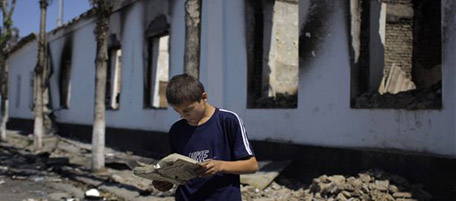 An ethnic Uzbek boy reads a fire damaged book near a burned school building in the Furkat district of Osh, southern Kyrgyzstan, Saturday, June 26, 2010. Kyrgyzstan holds a referendum on a new constitution Sunday, a risky gamble amid deadly ethnic tensions but one the interim government hopes will legitimize their hold on power until the region's first parliamentary democracy looks strikingly similar to the constitution drawn up by former President Kurmanbek Bakiyev, who was ousted in a bloody revolution three months ago. (AP Photo/Sergey Ponomarev)