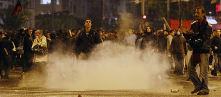 Protesters react as riot police throw tear gas during a demonstration in Athens, on Wednesday, Nov. 17, 2010. Youths hurled rocks, flares and smashed-up paving stones at police outside the U.S. Embassy in Athens, during a mass rally to mark the anniversary of a 1973 anti-dictatorship uprising. Riot police used tear gas and stun grenades, during the brief but violent confrontation with dozens of youths and chased groups that dispersed down streets near the embassy building. At least 40 people were detained by police, authorities said, while one protester was being treated in hospital for burns. More than 6,000 officers were on duty to police the annual march, which was generally peaceful. It was attended by more than 20,000 people. (AP Photo/Alkis Konstantinidis)