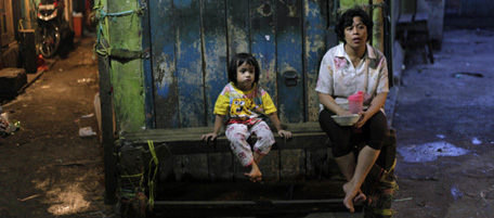 A woman sits with her daughter as she feeds her at dusk at a market in Jakarta, Indonesia, Wednesday, Jan. 19, 2011. (AP Photo/Dita Alangkara)