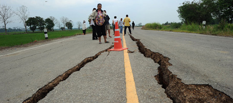 Thai villagers look at a damage road caused from the earthquake at Mae Sai district near the Thai-Myanmar border on March 26, 2011. Rescuers struggled to reach remote Myanmar towns hit by a powerful earthquake which killed 75 as rare images from the area showed roads torn apart and wooden homes reduced to piles of timber. AFP PHOTO/PORNCHAI KITTIWONGSAKUL (Photo credit should read PORNCHAI KITTIWONGSAKUL/AFP/Getty Images)