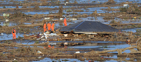 Rescue workers check the remains of a tsunami devestated house for people in Natori in Miyage prefecture on March 13, 2011. Japan battled a feared meltdown of two reactors at a quake-hit nuclear plant, as the full horror of the disaster emerged on the ravaged northeast coast where more than 10,000 were feared dead. An explosion at the ageing Fukushima No. 1 atomic plant blew apart the building housing one of its reactors on March 12, a day after the biggest quake ever recorded in Japan unleashed a monster 10-metre (33-foot) tsunami. AFP PHOTO/MIKE CLARKE (Photo credit should read MIKE CLARKE/AFP/Getty Images)