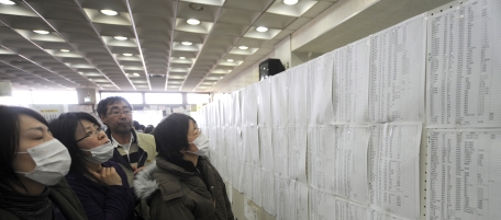 People check lists for survivors at an evacuation centre in in Natori City in Miyagi prefecture on March 14, 2011. A new explosion at a nuclear plant in nearby Fukushima prefecture hit punch-drunk Japan on March 14 as it raced to avert a reactor meltdown after a quake-tsunami disaster that is feared to have killed more than 10,000 people. AFP PHOTO/MIKE CLARKE (Photo credit should read MIKE CLARKE/AFP/Getty Images)