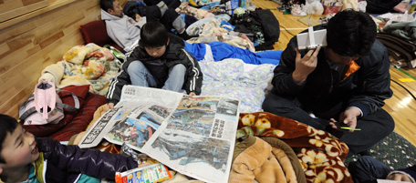 A young boy (C) reads a newspaper reporting on the earthquake at a shelter for evacuees in the town of Minamisoma in Fukushima Prefecture on March 12, 2011 a day after an 8.9 magnitude quake and tsunami devastated the region. An explosion and feared meltdown at a Japanese nuclear plant in Fukushima prefecture on March 12 exposed the scale of the disaster facing the country after the massive quake and tsunami left more than 1,000 dead. AFP PHOTO / KAZUHIRO NOGI (Photo credit should read KAZUHIRO NOGI/AFP/Getty Images)