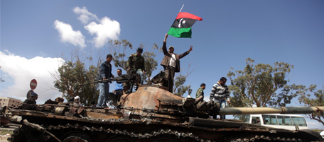 Libyan rebels wave their flag on top of a wrecked tank belonging to Moammer Khaddafi's forces on the western entrance of Benghazi on March 20, 2011. The initial part of an international operation to enforce a no-fly zone over Libya "has been successful" and the government's offensive on Benghazi has been stopped, top US military commander Michael Mullen said. AFP PHOTO/PATRICK BAZ (Photo credit should read PATRICK BAZ/AFP/Getty Images)