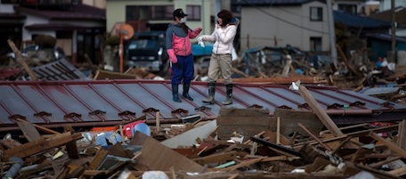 Tsunami survivor Yuka Matsukawa (R) meets a friend Reina Itakura (L) on the roof of a wrecked house in a sea of debris in Higashimatsushima, Miyagi prefecture, on April 3, 2011. The wider search for victims of the huge earthquake and resulting tsunami on March 11 continued along the disaster-ravaged coast -- joined by 18,000 Japanese military personnel and 7,000 US forces, as well as police, firefighters and coastguard rescue and dive teams. There are still over 15,000 people missing since the twin disaster. AFP PHOTO / YASUYOSHI CHIBA (Photo credit should read YASUYOSHI CHIBA/AFP/Getty Images)