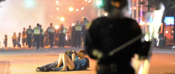 VANCOUVER, BC - JUNE 15: Riot police walk in the street as a couple kiss on June 15, 2011 in Vancouver, Canada. Vancouver broke out in riots after their hockey team the Vancouver Canucks lost in Game Seven of the Stanley Cup Finals. (Photo by Rich Lam/Getty Images)