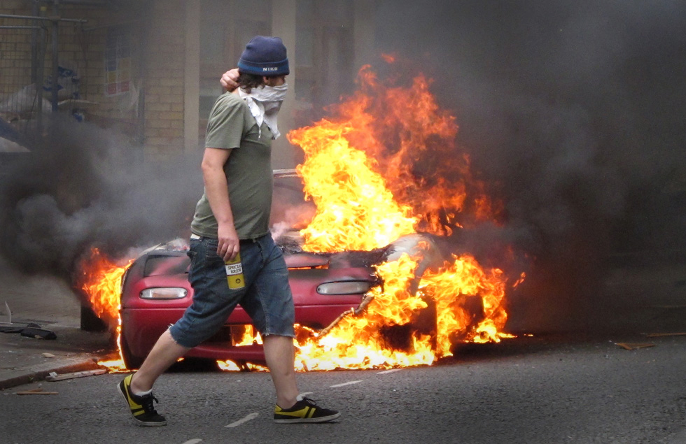 Un giovane mascherato davanti a un'auto data alle fiamme a Hackney (Peter Macdiarmid/Getty Images)
