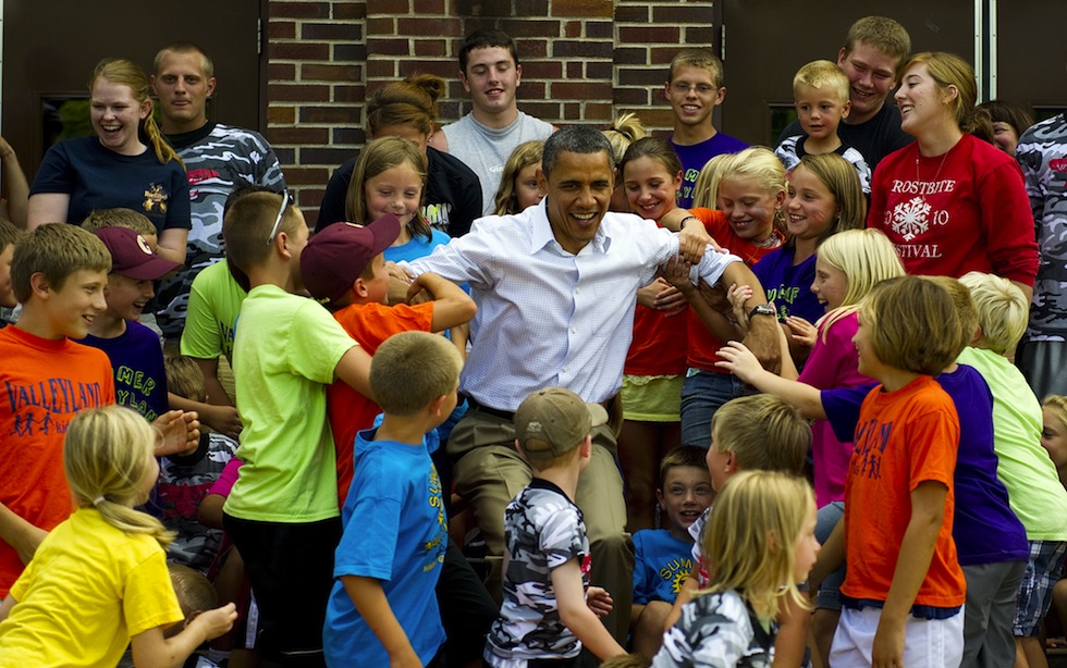 Studenti del campo estivo della scuola pubblica di Chatfield, in Minnesota, aiutano Barack Obama a rialzarsi dopo aver scattato una foto insieme davanti alla scuola, 15 agosto 2011. (JIM WATSON/AFP/Getty Images)