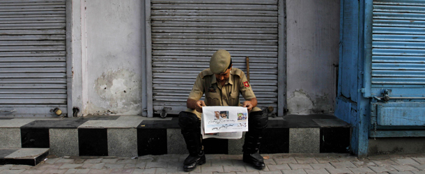 An Indian policeman reads a newspaper outside closed shops during a strike in Srinagar, India, Monday, Aug. 15, 2011. India marked 64 years of independence from British rule. (AP Photo/Mukhtar Khan)