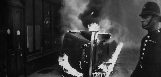 circa 1936: A policeman stands by a burning car, set alight during a communist march in the East End of London. (Photo by Topical Press Agency/Getty Images)