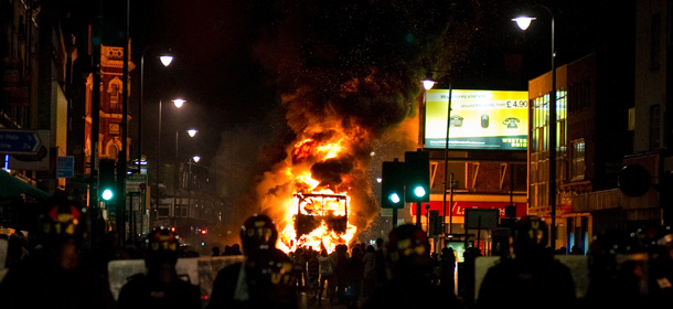 A double decker bus burns as riot police try to contain a large group of people on a main road in Tottenham, north London on August 6, 2011. Two police cars were on Saturday set ablaze in north London following a protest over the fatal shooting of a 29-year-old man in an armed stand-off with officers. The patrol cars were torched as dozens gathered outside the police station on the High Road in Tottenham. AFP PHOTO/LEON NEAL (Photo credit should read LEON NEAL/AFP/Getty Images)