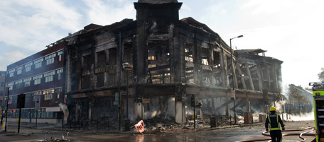 Firefights survey the burnt-out shell of a carpet showroom on High Road in Tottenham, north London on August 7, 2011. Two police cars and a large number of buildings were on Saturday set ablaze in north London following a protest over the fatal shooting of a 29-year-old man in an armed stand-off with officers. The patrol cars were torched as dozens gathered outside the police station on the High Road in Tottenham.AFP PHOTO/LEON NEAL (Photo credit should read LEON NEAL/AFP/Getty Images)