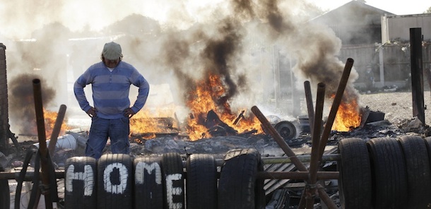 An Irish traveller resident looks down as he pauses whilst throwing items onto a fire forming a barricade, during evictions at the Dale Farm travellers site near Basildon, England, 30 miles (50 kilometers) east of London, Wednesday, Oct. 19, 2011. British police in riot gear used sledgehammers to clear the way for the eviction of a community of Irish travellers from a site where they have lived illegally for a decade. A large force of police and bailiffs faced resistance from several dozen residents and supporters who threw bricks and struggled with officers. (AP Photo/Matt Dunham)
