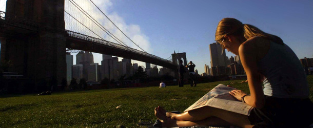 394507 06: Yvette Lenhart takes in some sun while reading a newspaper beneath the Brooklyn Bridge and still smoky Manhattan skyline five days after the World Trade Center attack September 16, 2001 in the Brooklyn borough of New York City. (Photo by Mario Tama/Getty Images)
