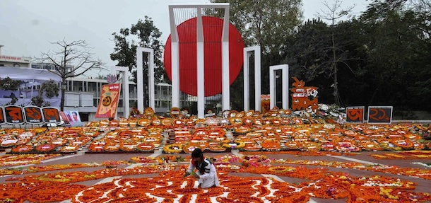 Bangladesh&#8217;s Language Movement martyrs monument is covered with floral tributes as a Bangladeshi youth adds the finishing touches to a display in Dhaka on February 21, 2011, to pay homage to the martyrs of the 1952 Bengali Language Movement. Tens of thousands of mourners walking barefoot thronged the memorial for the annual traditional remembrance of those killed when police fired on campaigners on this day in 1952, who were demanding Bengali be declared as one of the state languages of what was then Pakistan. AFP PHOTO/ STRINGER (Photo credit should read STRINGER/AFP/Getty Images)
