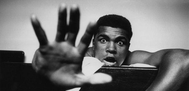 27th May 1963: American Heavyweight boxer Cassius Clay (later Muhammad Ali) lying on his hotel bed in London. He holds up five fingers in a prediction of how many rounds it will take him to knock out British boxer Henry Cooper. (Photo by Len Trievnor/Express/Getty Images)