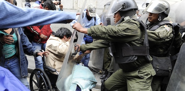 Activiststs taking part in a protest of impaired people struggle with riot police as they try to get to the Plaza de Armas square in La Paz, on February 23, 2012. Around 80 people with reduced capabilities marched 1,600 km (1,000 miles) on wheelchairs to the capital demanding a 3,000 Bolivianos (USD 437) annual bonus and a law of special treatment. AFP PHOTO/Jorge Bernal (Photo credit should read JORGE BERNAL/AFP/Getty Images)