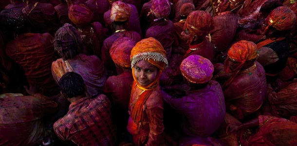 A child looks on as Indian villagers smear themselves with colours during the Lathmar Holi festival at the Nandji Temple in Nandgaon, some 120 kms from New Delhi, on March 3, 2012. The women of Nandgaon, the hometown of Hindu God Krishna, attack the men from Barsana, the legendary hometown of Radha, consort of Hindu God Krishna, with wooden sticks in response to their efforts to put color on them, reciprocating acts performed yesterday in Barsana between the women of that village with the men of Nandgaon as they observe the Lathmar Holi festival. AFP PHOTO/ Manan VATSYAYANA (Photo credit should read MANAN VATSYAYANA/AFP/Getty Images)