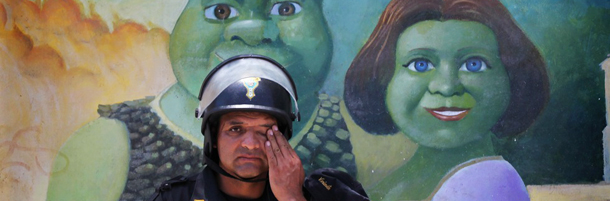 A riot police wipes his brow in front of a mural of the animated film characters Shrek and Princess Fiona, during a demonstration against the Conga gold and silver mining project in Huacho, Peru, Wednesday Feb. 8, 2012. Demonstrators in Peru resumed their protests against plans to develop a $4.8 billion gold mine, saying they fear that the Conga mine, which would produce gold and copper as well as silver, will taint their water and affect a major aquifer. The Newmont Mining Corporation, based in the U.S., owns a majority share of the mine. (AP Photo/Martin Mejia)