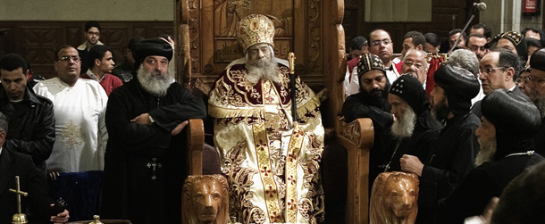 Egyptian Coptic priests gather around the body of Pope Shenuda III, the spiritual leader of the Middle East's largest Christian minority, sitting dressed in formal robes on a wooden throne at the Saint Mark's Coptic Cathedral in Cairo's al-Abbassiya district on March 19, 2012. Pope Shenuda died at the age of 88, after a long battle with illness and based on his wishes he will be buried on March 20, at St. Bishoy monastery in Wadi Natrun in the Nile Delta where he spent his time in exile after a dispute with late president Anwar Sadat.AFP PHOTO/GIANLUIGI GUERCIA (Photo credit should read GIANLUIGI GUERCIA/AFP/Getty Images)