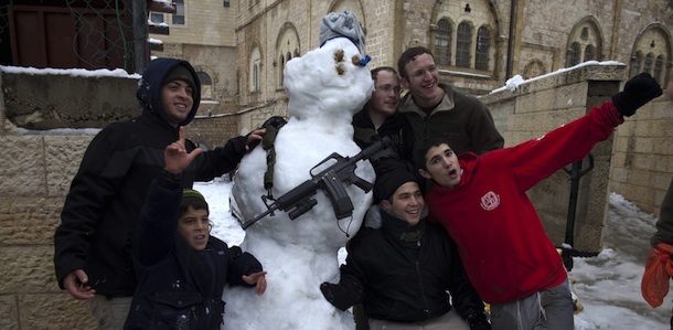 Jewish settlers pose for a picture with a snowman armed with an M-16 rifle in the West Bank city of Hebron as wintry weather swept through the region on March 2, 2012. AFP PHOTO/MENAHEM KAHANA (Photo credit should read MENAHEM KAHANA/AFP/Getty Images)
