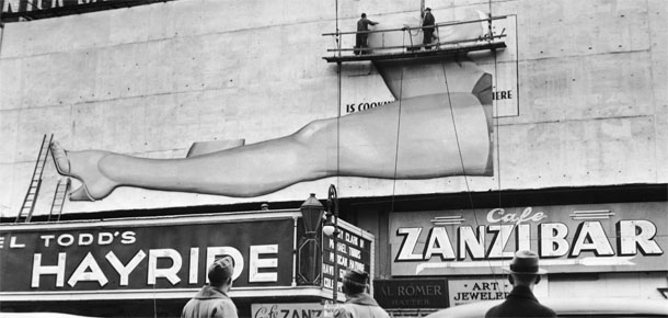 Two American soldiers and a civilian in a fedora watch workers on a scaffold hang a billboard advertisement featuring a woman's bare legs above the Winter Garden Theater and Cafe Zanzibar, Broadway, New York, 1944. (Photo by Hulton Archive/Getty Images)