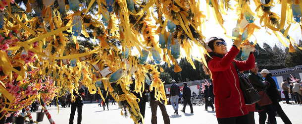 A chinese women tied yellow ribbons to a tree during Qingming Festival (Tomb-sweeping Day) in Beijing, China, Wednesday, April 4, 2012. Qingming festival, also known as the Grave Sweeping Day is a day when Chinese around the world remember their dearly departed and take time off to clean up the tombs and place flowers and offerings. (AP Photo/ Vincent Thian)