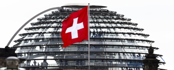 The Swiss national flag on top of Switzerland's embassy waves in the wind in front of the glass dome of the Reichstag building which host German Parliament in Berlin, Monday, April 2, 2012. Last week Swiss authorities have issued arrest warrants for three German tax inspectors over the purchase in 2010 of a CD containing data on suspected tax cheats. (AP Photo/Markus Schreiber)