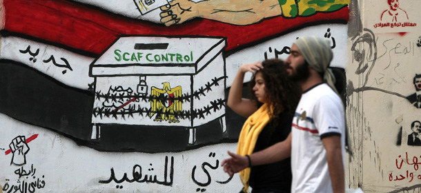 Egyptians walk past graffiti depicting a chained ballot box being controlled by the ruling military council at Tahrir Square in Cairo on May 25, 2012. Egyptians reacted nervously to the first results of their presidential vote, some celebrating the successful election, and others horrified by the strength of Muslim Brotherhood and ex-regime candidates. AFP PHOTO/MAHMUD HAMS (Photo credit should read MAHMUD HAMS/AFP/GettyImages)