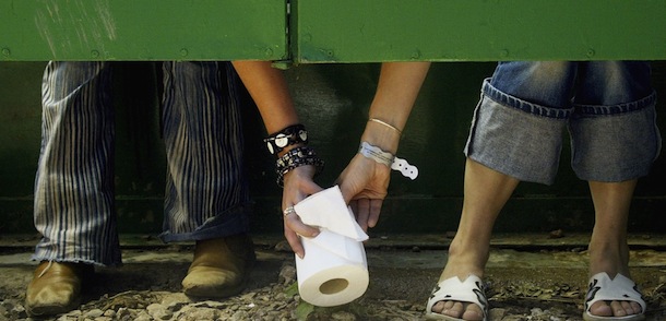 SOMERSET, ENGLAND - JUNE 25: Two festival-goers pass a roll of toilet paper between toilet cubicles, during the 2004 Glastonbury Festival on June 25, 2004 at Worthy Farm, Pilton, Somerset, England. The music festival spans over 3 days and runs until June 27. (Photo by Matt Cardy/Getty Images)