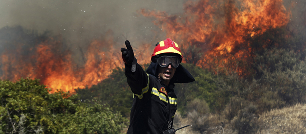 A firefighter gestures instructions to his colleagues as a fire rages in Palea Fokaia, south of Athens, Saturday, June 16, 2012. A fire aided by strong winds has burned grassland and threatened houses near the town of Keratea, 50 kilometers (30 miles) south of Athens. The fire started in the early Saturday afternoon on dried grass, apparently as the result of an accident and has been spreading fast, threatening to engulf isolated houses on the outskirts of the towns of Keratea and Palea Fokaia. (AP Photo/Kostas Tsironis)