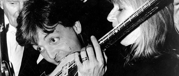 Fomer Beatle Paul McCartney bites into a 4-string bass guitar cake during a luncheon at Claridge's in London, England, Tuesday, Dec. 20, 1989. McCartney received a Performing Right Society Award, held by an unidentified man at left, in recognition of his unique contribution to British music. At right is Linda McCartney. (AP Photo)