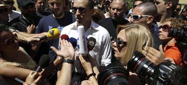 The spokesman of Greece's extreme-right Golden Dawn party Ilias Kasidiaris, center, escorted by party members talks to media outside the prosecutor's office in Athens, Monday June, 11, 2012. Kasidiaris who caused uproar last week by hitting one politician and throwing a glass of water over another during a live TV news program, on Monday sued the two candidates and the television channel that hosted the show. He appeared at an Athens court to submit lawsuits against Communist Party candidate Liana Kanelli and Syriza party member Rena Dourou for unprovoked insult and against Antenna television for illegal detention. (AP Photo/Petros Karadjias)