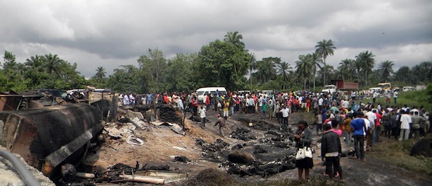 People gather at the scene where a Nigerian petrol tanker tipped over and pools of spilled oil caught fire in Okogbe on July 12, 2012. More than 100 people who rushed to scoop up fuel after a Nigerian petrol tanker tipped over on July 12 were killed when the vehicle and pools of spilled oil caught fire. Children were among those killed, while dozens more were badly burned, despite a warning from troops who arrived at the crash site that a blaze could ignite at any moment. AFP PHOTO/STR (Photo credit should read STR/AFP/GettyImages)