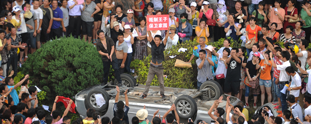 A man holds a placard as he stands on a car overturned by a group of protestors near the local government office compound in the coastal city of Qidong, near Shanghai, in the eastern China province of Jiangsu on July 28, 2012. Thousands of demonstrators protesting against alleged pollution from a paper factory in east China clashed with police, an AFP photographer said. AFP PHOTO/Peter PARKS (Photo credit should read PETER PARKS/AFP/GettyImages)