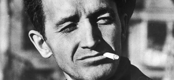 Headshot of American singer and musician Woody Guthrie (1912 - 1967) smoking a cigarette and squinting outdoors, c. 1960. He wears a fishing cap, turtleneck sweater, and a peacoat. (Photo by Getty Images)