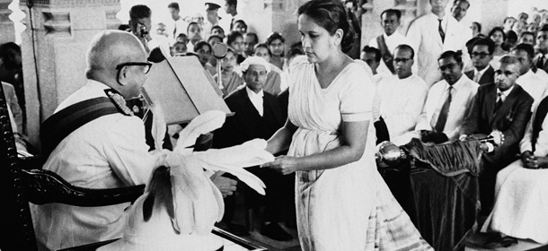 The Prime Minister of Ceylon, Mrs. Sirimavo Bandaranaike, hands over a copy of the throne speech to Sir Oliver Goonetilleke, the Governor General of Ceylon, at the ceremonial inauguration of the New Ceylon Parliament in Colombo on August 12, 1960. In the centre background wearing a wig and gown, is Ralph Deraniyagala clerk of the Ceylon House of Representatives. At right are (left to right) T.B. Ilangaratne the minister of trade: Felix Dias Bandaranaike minister of finance: and Dudley Senanayake, leader of the opposition (wearing a dark suit). (AP Photo)