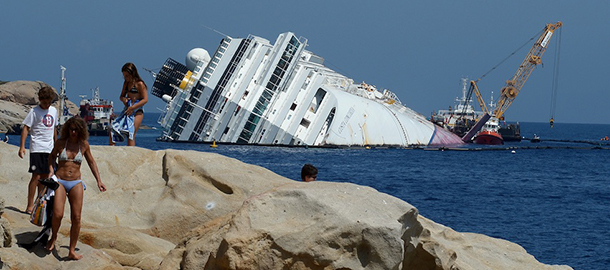 Tourists sunbathe as salvage team members work at the rock on the side of the Costa Concordia cruise ship near the harbour of Giglio Porto on July 12, 2012. Salvage crews began work on preparations to refloat the half-submerged Costa Concordia cruise liner in what is set to be the biggest ever operation of its kind. The cruise liner, operated by Carnival Corp's Costa Cruises unit, capsized off the Tuscan island of Giglio after hitting rocks on January 13. At least 30 people died and two are still unaccounted for. AFP PHOTO/ VINCENZO PINTO (Photo credit should read VINCENZO PINTO/AFP/GettyImages)