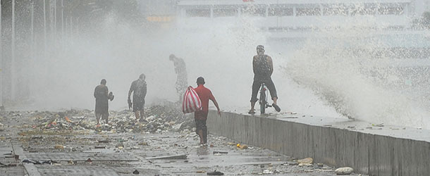 People walk past high waves breaking into the promenade of the famous Roxas boulevard in Manila on July 30, 2012, as strong winds and rains due to Tropical Storm Saola hit the capital. At least one person was killed and millions were left without power on July 30, as Tropical Storm Saola brought heavy rains to large parts of the Philippines, the government said. AFP PHOTO / TED ALJIBE (Photo credit should read TED ALJIBE/AFP/GettyImages)