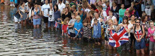 LONDON, ENGLAND - JULY 27: Crowds enter the water to watch the Queen's rowbarge 'Gloriana' carry the Olympic flame along the river Thames from Hampton Court to City Hall on the final day of the London 2012 Olympic Torch Relay on July 27, 2012 in London, England. The Olympic flame is making its way through the capital on the final day of its journey around the UK before arriving in the Olympic Stadium tonight for the Olympic games' Opening Ceremony. (Photo by Oli Scarff/Getty Images)