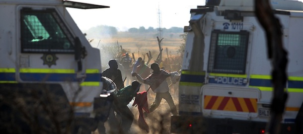 Striking mineworkers throw stones as police open fire on striking miners at the Lonmin Platinum Mine near Rustenburg, South Africa, Thursday, Aug. 16, 2012. South African police opened fire Thursday on a crowd of striking workers at a platinum mine, leaving an unknown number of people injured and possibly dead. Motionless bodies lay on the ground in pools of blood. (AP Photo)