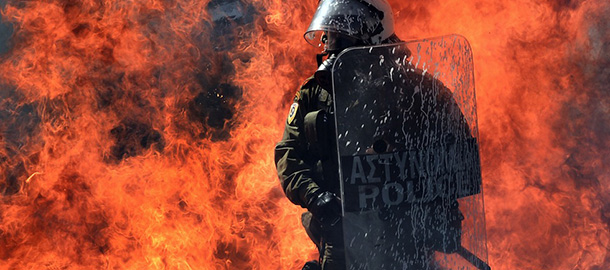 A fire bomb explodes behind a riot police squad on September 26, 2012 in Athens during clashes with demonstrators at a 24-hours general strike. Police in Athens clashed with hooded youths throwing firebombs on the sidelines of a large demonstration against a new round of austerity cuts. AFP PHOTO / ARIS MESSINIS (Photo credit should read ARIS MESSINIS/AFP/GettyImages)
