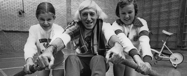 English dj and television presenter Jimmy Savile (1926 &#8211; 2011), with pupils Christine Swan and Lesley Faulkner at the William Gladstone High School in Brent, London, 20th October 1977. Savile is at the school to make part of a film on vandalism for Northern Ireland. (Photo by Colin Davey/Evening Standard/Hulton Archive/Getty Images)
