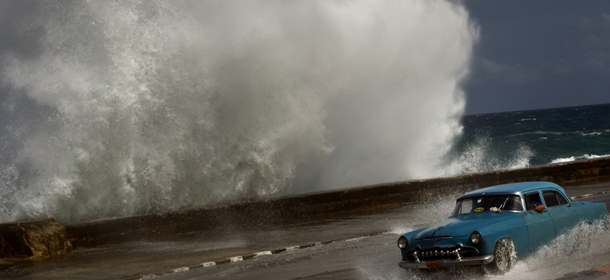 A driver maneuvers his classic American car along a wet road as a wave crashes against the Malecon in Havana, Cuba, Thursday, Oct. 25, 2012. Hurricane Sandy blasted across eastern Cuba on Thursday as a potent Category 2 storm and headed for the Bahamas after causing at least two deaths in the Caribbean. (AP Photo/Ramon Espinosa)
