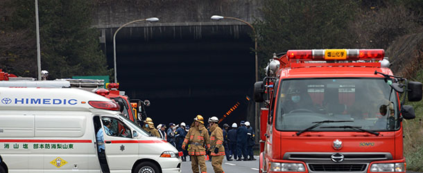 Rescue workers and policeman gather alongside emergency services vehicles on the road leading to the entrance of the collapsed Sasago tunnel on the Chuo expressway in Koshu city, Yamanashi prefecture, some 80-kilometres west of Tokyo on December 2, 2012. At least seven people are missing after concrete ceiling panels along a section of highway tunnel collapsed in Japan on December 2. AFP PHOTO / Yoshikazu TSUNO (Photo credit should read YOSHIKAZU TSUNO/AFP/Getty Images)
