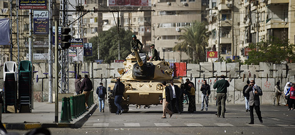 An Egyptian army tank is deployed near the presidential palace in Cairo as opposition supporters and people walk by on December 10, 2012. President Mohamed Morsi has ordered Egypt&#8217;s army to &#8220;cooperate&#8221; with police and given it powers of arrest until the results of a referendum to be held this weekend, according to a decree obtained by AFP. AFP PHOTO/GIANLUIGI GUERCIA (Photo credit should read GIANLUIGI GUERCIA/AFP/Getty Images)
