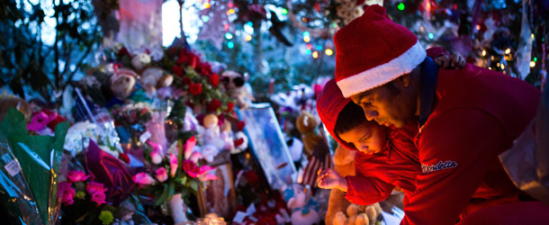 NEWTOWN, CT &#8211; DECEMBER 24: Claud Oliveira holds his son, Jeremiah Oliveira, while lighting a candle at a memorial for those killed in the school shooting at Sandy Hook Elementary School on December 24, 2012 in Newtown, Connecticut. Donations and letters are pouring in from across the country as the town tries to recover from the massacre. (Photo by Andrew Burton/Getty Images)
