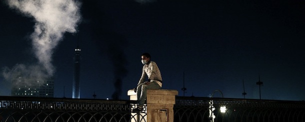 CAIRO, EGYPT - JANUARY 27: An Egyptian protester sits on a fence underneath a cloud of tear gas during clashes with riot police near Tahrir Square on January 27, 2013 in Cairo, Egypt. Violent protests continued across Egypt two days after the second anniversary of the Egyptian Revolution that overthrew former President Hosni Mubarak on January 25, and one day after the announcement of the death penalty for 21 suspects in connection with a football stadium massacre one year before. The verdict was announced in a case over the deaths of more than seventy fans of Egypt's Al-Ahly football club in a stadium massacre on February 1, 2012, in the northern city of Port Said, during a brawl that began minutes after the final whistle of a match between Al-Ahly and opposing side, Al-Masry. 21 fans of the opposing side, Al-Masry, were given the death penalty, a verdict that must now be approved by Egypt's Grand Mufti. (Photo by Ed Giles/Getty Images).